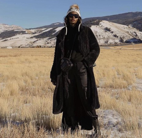 A young woman dressed in black in a steppe in front of some mountains.