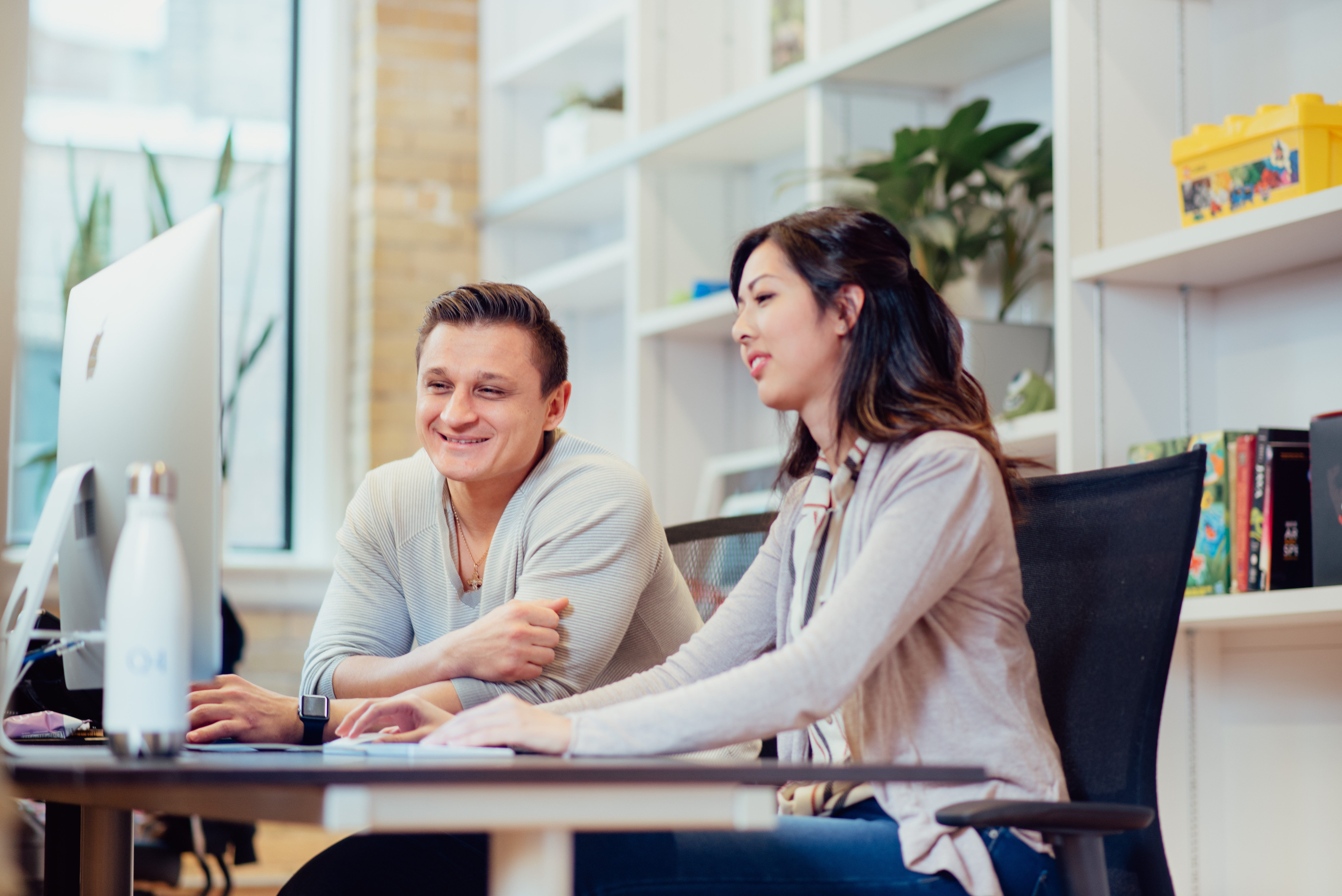 Alex and another young worker collaborate at a computer in a modern office.