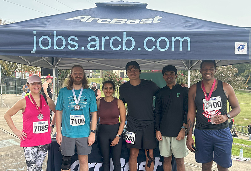 A group of volunteers wearing matching volunteer shirts, gathered behind a table in a lush green setting, ready to make a positive impact